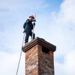 Chimney sweep standing on chimney with pole inside for cleaning.