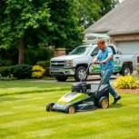 Professional lawn care service with man mowing green yard, truck nearby.