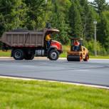 Paving company at work: dump truck, men smoothing pavement, and roller operator.